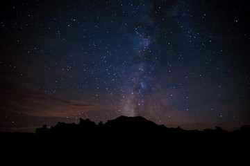 The Milky Way appears to erupt from a peak silhouetted against a starry sky in the Bisti Badlands...