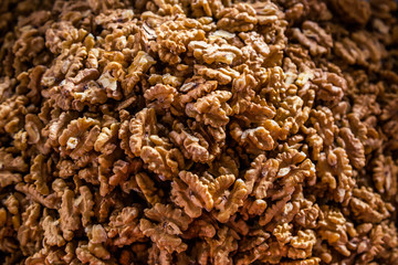 Many walnuts lie on the market and in the store. Open and peeled nuts are full of vitamins, a fresh and healthy snack for vegetarians. Shelled nuts in curved forms. Big plates on the market.