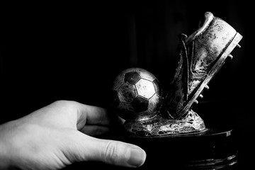Black and white Closeup of man hand holding metal football soccer winning trophy that has achieved it