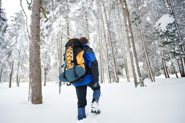 Young male mountain climber hiking through deep powder snow in a forest, wearing heavy backpack...