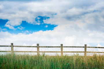 Closeup of very beautiful landscape view with Wooden fence in a green field against blue cloudy sky .