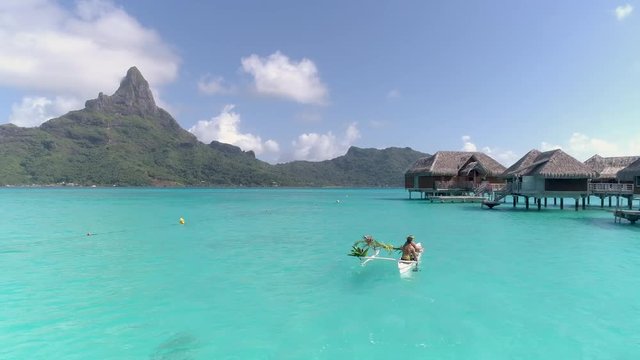 Aerial - Couple being transported with outrigger canoe to overwater villa
