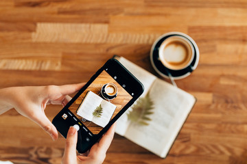 The girl is holding a phone and photographing the composition on the table