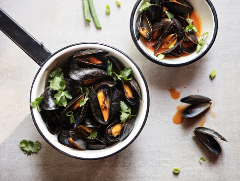 Curried Mussels are prepared in a white enamelware pot and bowl on a white surface.