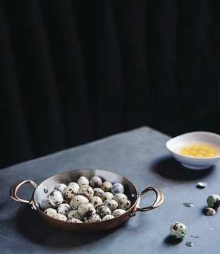 Quail eggs rest in a bowl on a gray table.