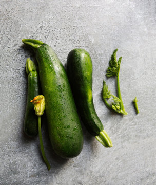 Zucchini squash and zucchini blossoms rest on a gray metal surface.