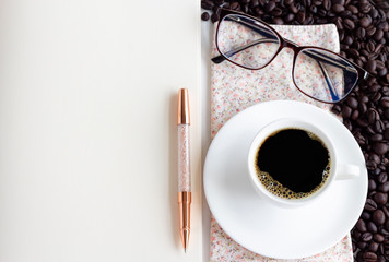 A cup of white coffee, pen, and glasses are placed on bright pink cloth.  The concept of leisure with writing or drawing in a notebook.