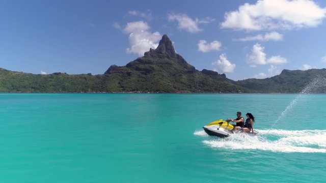 Aerial - Tracking shot of couple riding jet ski in luxury Bora Bora resort
