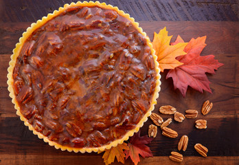Happy Thanksgiving traditional pecan pie on vintage dark wood table and background with autumn leaves. 