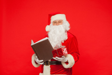 Naklejka premium Santa Claus reads old book, on a red background. Christmas
