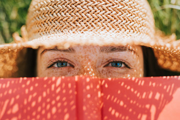 Closeup of woman covering her face with a red book - obrazy, fototapety, plakaty