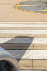 Closeup of jet engine with wing shadow on striped runway