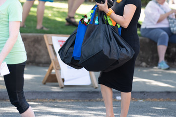 Woman dressed in black dress holding lots of bags in her hands on the street.