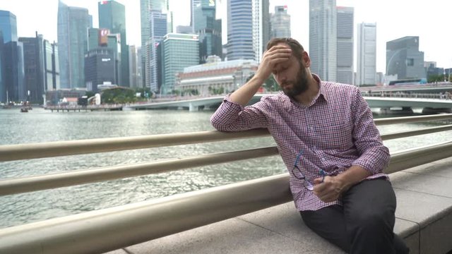 Sad, unhappy man sitting by river in the city