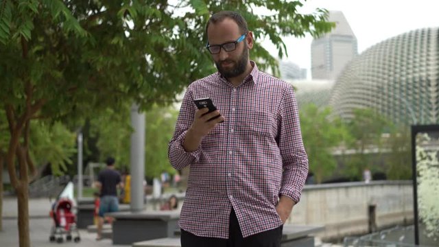 Young man texting on smartphone standing in city park