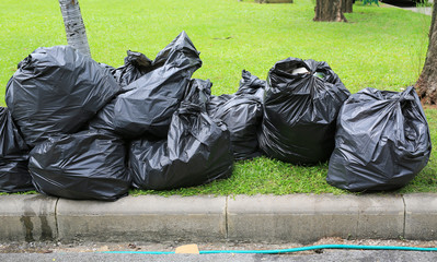 Black Plastic trash bags on green grass garden near street.