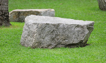 Rock seat on green grass garden. Natural stone chair in park.