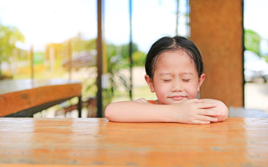 Closed eyes and smiling little Asian kid girl lying on the wooden table.