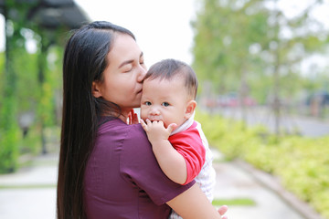 Portrait of Infant baby boy is sucking finger with Asian mother carrying.