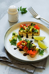 Avocado and salmon sandwiches with balsamic sauce and cilantro on old olive board. Top view.