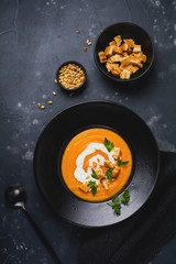 Pumpkin soup in black ceramic plate on dark wooden background. Traditional autumn food. Top view copy space.