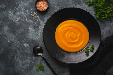 Pumpkin soup in black ceramic plate on dark wooden background. Traditional autumn food. Top view copy space.