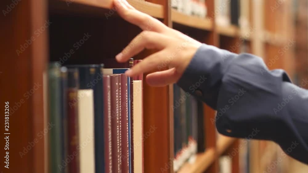 Poster a man searching and browsing books in a library. picks up and takes a book from a shelf. pile of boo