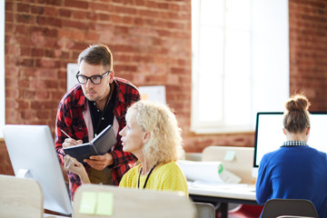 Mature employer consulting one of subordinates in front of computer monitor in office