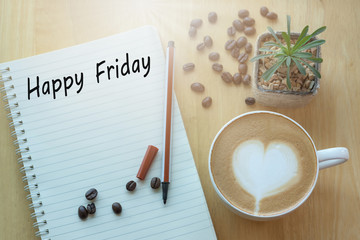 Concept Happy firday message on notebook, pencil and coffee cup on wooden table.