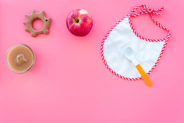 Baby food concept. Apple puree in bowl near bib, apple, spoon on pink background top view space for text