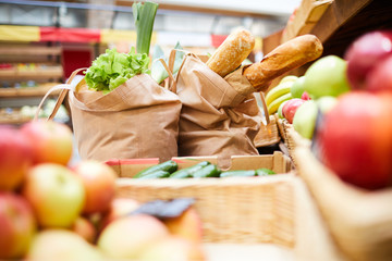 Close-up of shopping bags full of fresh products such like bread vegetables and greens on counter