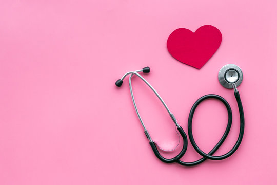 Heart disease concept. Stethoscope near heart sign on pink background top view copy space