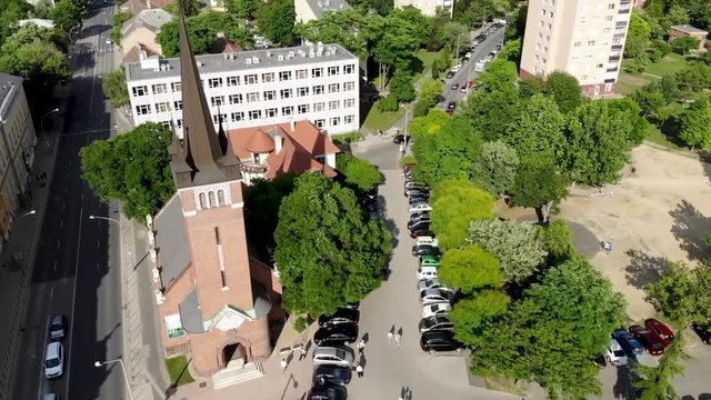 Moving towards a church made of bricks by a car park and lush green trees
