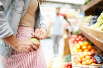Deurstickers Close-up of unrecognizable woman in stripped skirt hiding apple in pocket while stealing it in food store © pressmaster