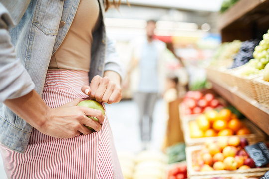 Close-up of unrecognizable woman in stripped skirt hiding apple in pocket while stealing it in food store