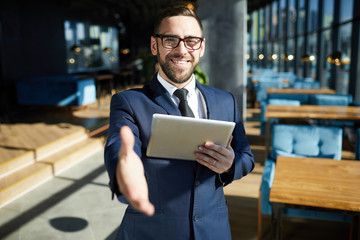 Businessman with toothy smile holding touchpad in one hand while giving the other one to client of...