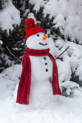 snowman in the forest in Christmas clothes, next to the tree