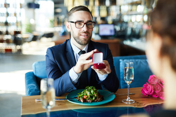 Young man in elegant suit offering girlfriend to be his wife during lunch in restaurant