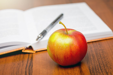 Red ripe apple near open book. Eating in a break between occupation_
