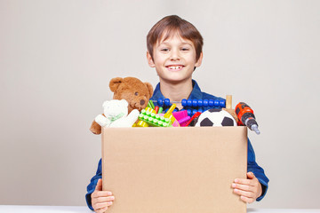 Donation concept. Kid holding donate box with clothes, books, school supplies and toys
