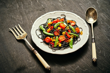 fresh delicious black vegan spaghetti with cherry tomatoes, chili pepper, on a white plate