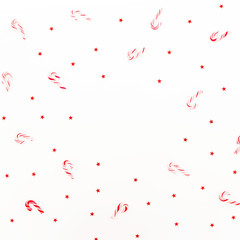 Fototapeta na wymiar Christmas frame pattern of candy cane and red shiny confetti on white background. Flat lay, top view.