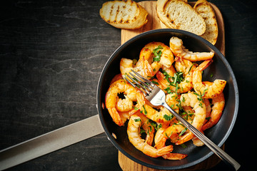 fresh delicious fried tiger prawns in a pan and toasts on wooden board