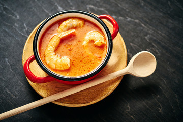 traditional Thai soup with shrimp and coconut milk in a red pot and a wooden spoon