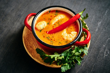 traditional Thai soup with shrimp and coconut milk in a red pot with parsley and chilli pepper