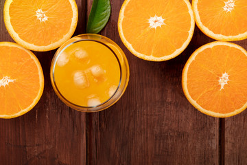 An overhead photo of a glass of fresh orange juice with orange halves, shot from the top on a dark rustic wooden background with copy space