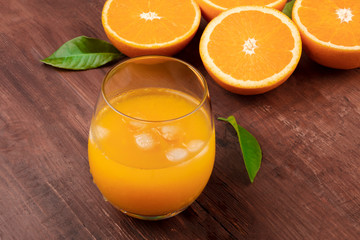 A photo of a glass of fresh orange juice with orange halves and green leaves on a dark rustic wooden background with copy space