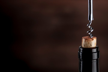 A closeup of a corkscrew pulling a cork from a bottle of wine on a dark background with a place for...