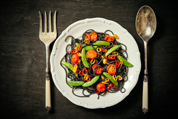 fresh delicious black vegan spaghetti with cherry tomatoes, chili pepper, on a white plate