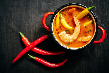 traditional Thai soup with shrimp and coconut milk in a red pot and chilli pepper